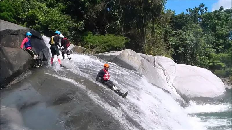 Guests riding a long natural rock waterslide into a river pool, El Yunque canyon, Puerto Rico