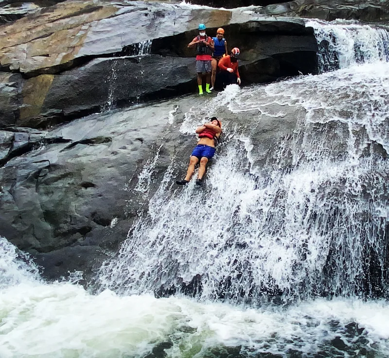 Two guests on a natural rock slide into a river pool, El Yunque, Puerto Rico