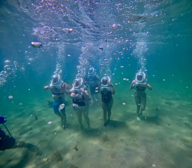 Group walking the sea floor in helmet diving gear with reef fish around them, San Juan, Puerto Rico