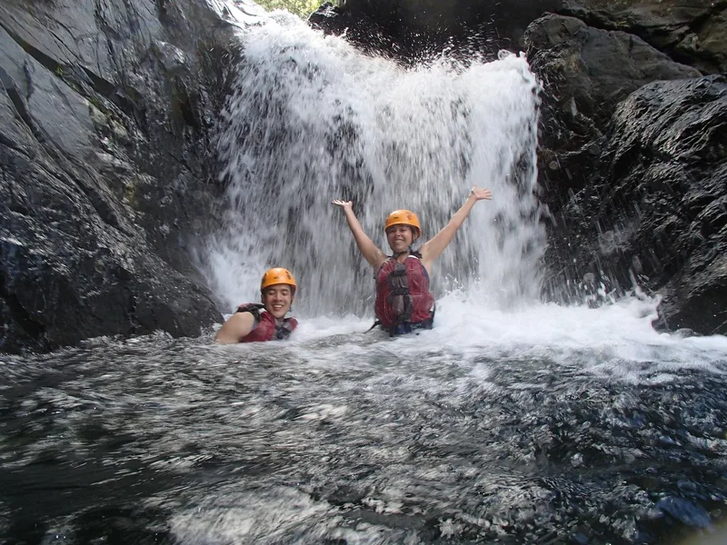 Guest swimming in a natural pool beneath an El Yunque waterfall
