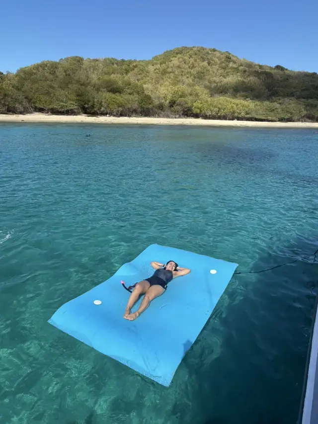 Guest relaxing on a floating mat in clear turquoise water beside an island