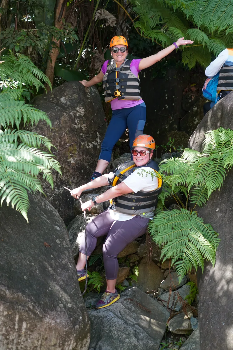 Two harnessed climbers on a rock ledge among ferns, via ferrata, south side of El Yunque, Puerto Rico