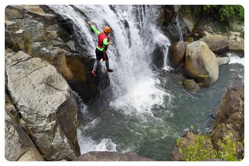 Hiker climbing down beside a waterfall into a boulder-lined pool, El Yunque rainforest, Puerto Rico