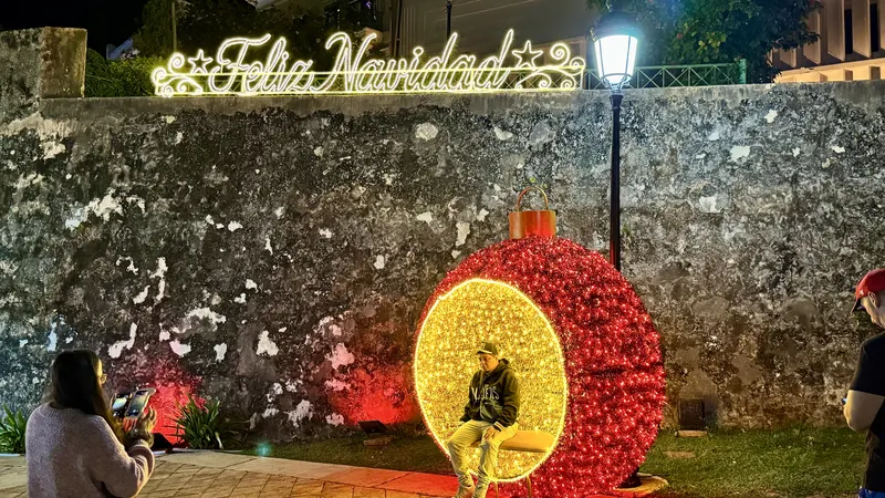 Feliz Navidad lights above a giant red ornament photo spot on an old stone wall in Puerto Rico